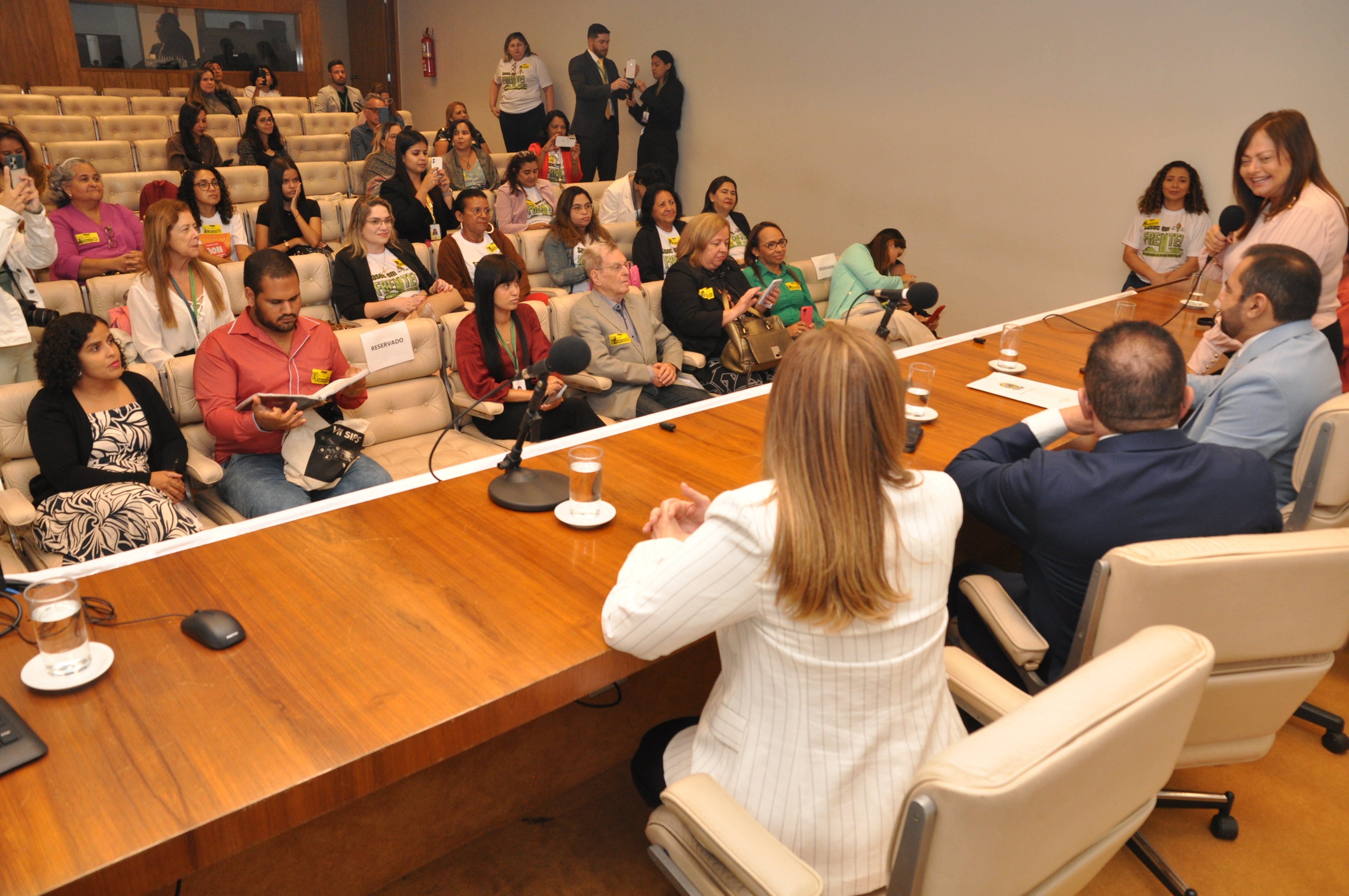 Imagem mostra a mesa do evento de costas com as pessoas sentadas no auditório.