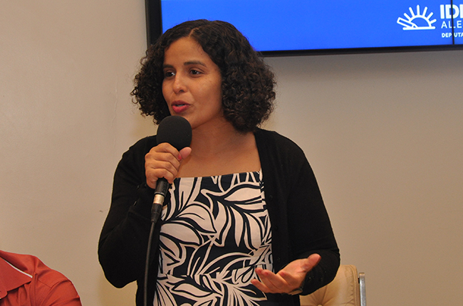 Imagem mostra a conselheira do CFESS Alana Rodrigues em pé durante a fala na mesa.